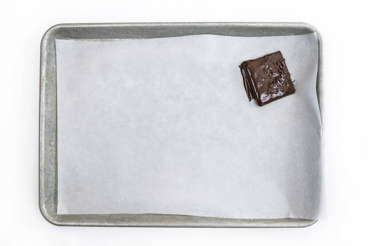 A chocolate covered graham cracker on a baking sheet lined with parchment paper.