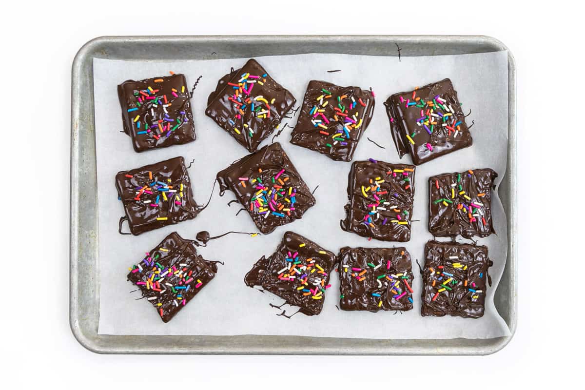Twelve chocolate covered graham cracker squares on a baking sheet lined with parchment paper.