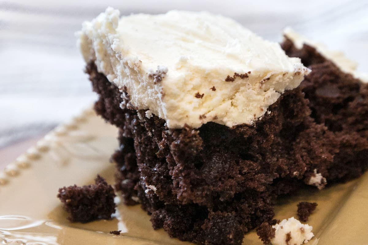 A slice of chocolate cake with white chocolate buttercream frosting on it.