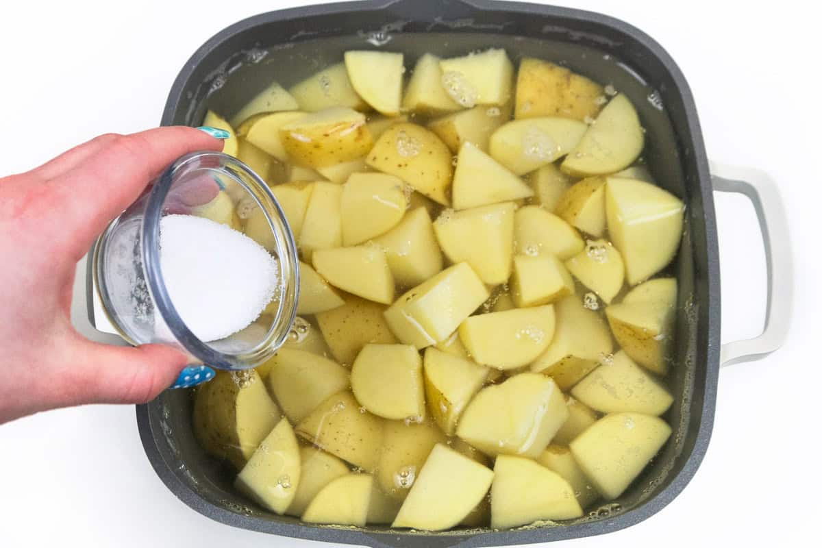 Salt added to cut potatoes in a saucepan with water.