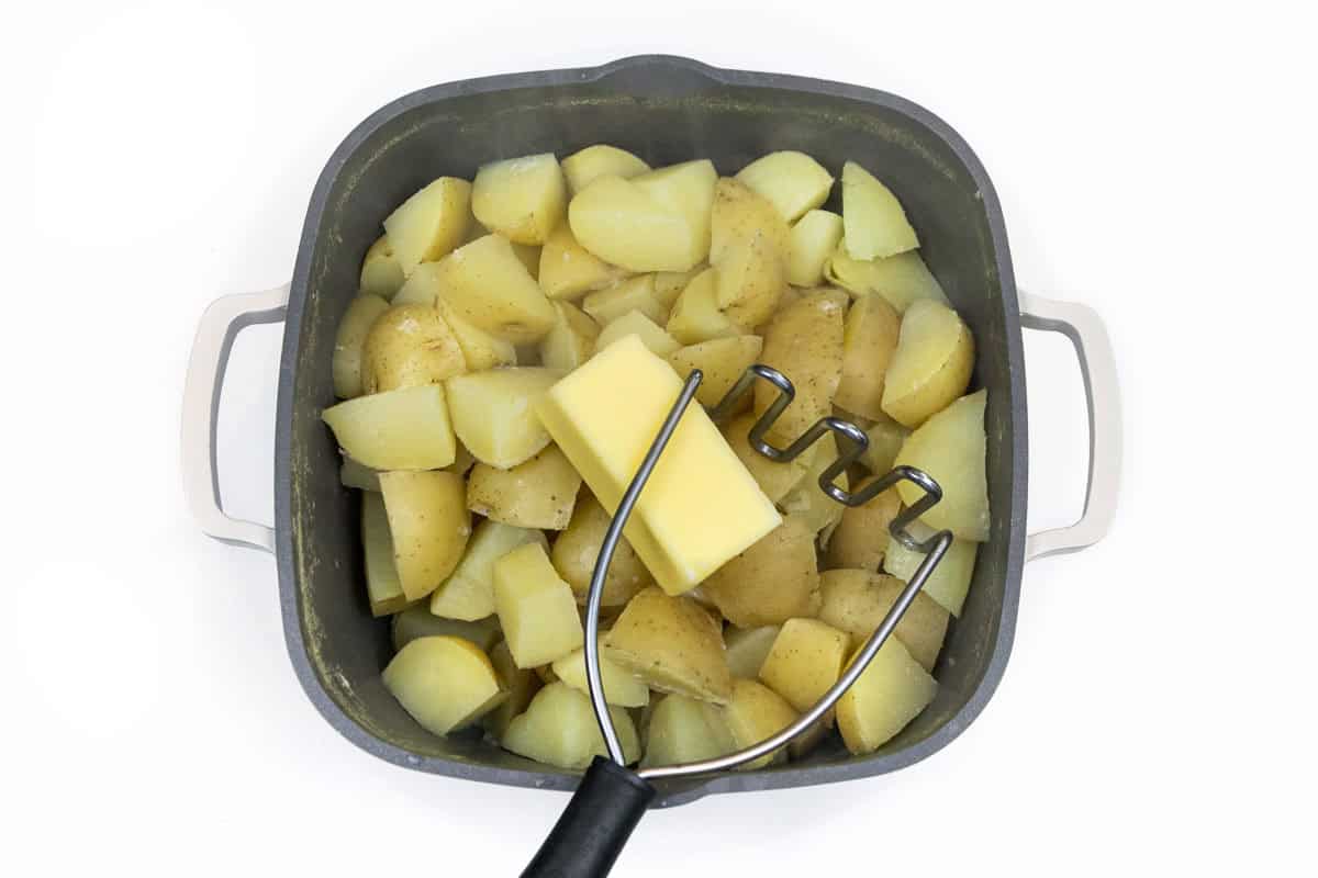 Add butter to cooked potatoes in saucepan.