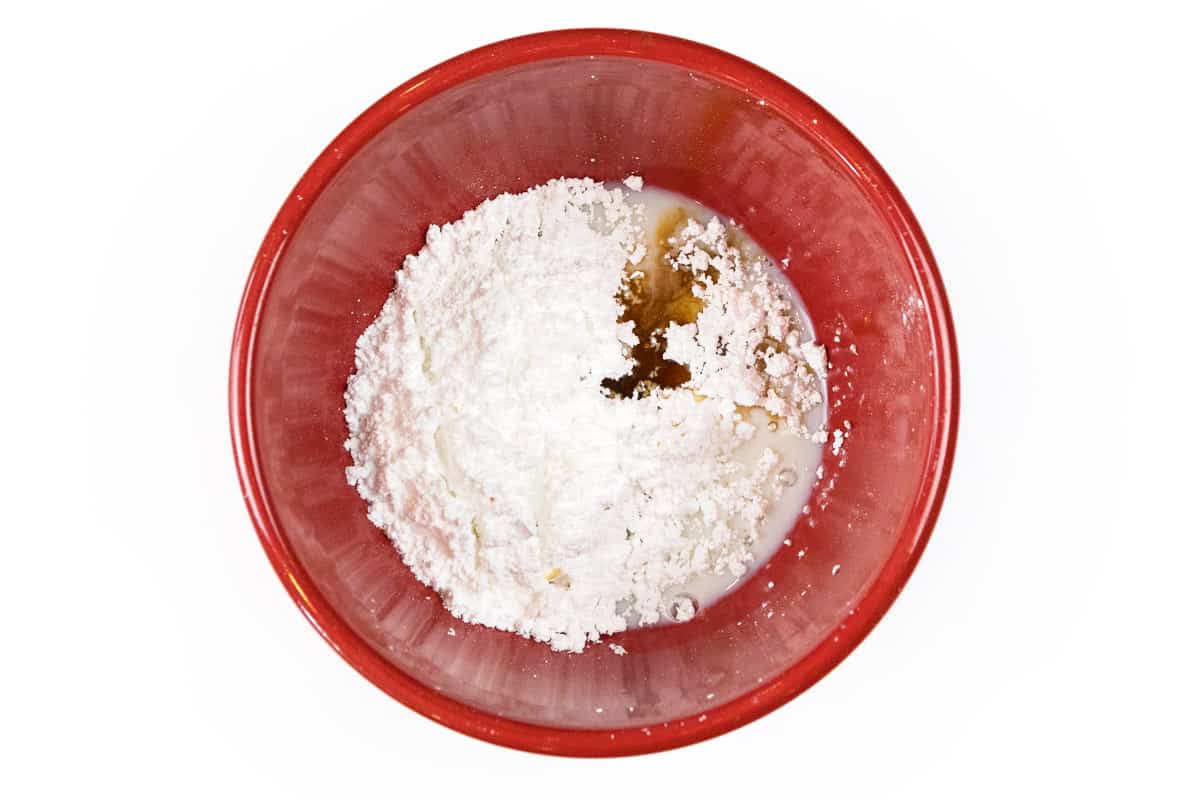 Powdered sugar, milk, and vanilla extract are added to a bowl.