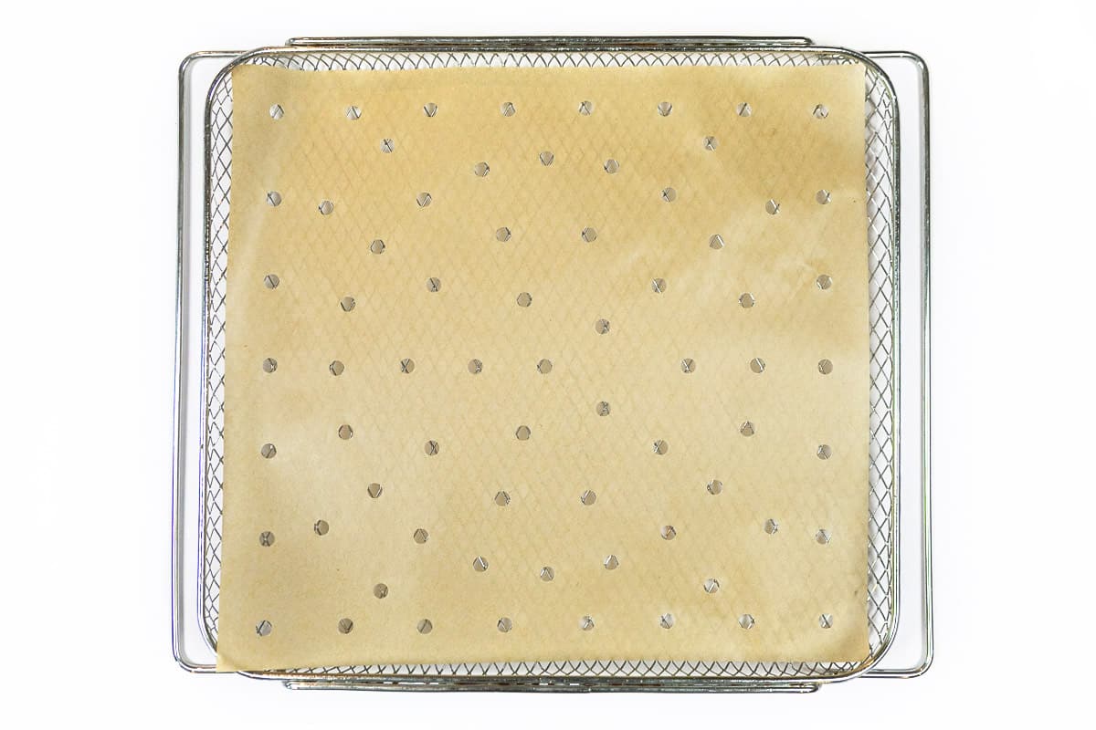 Parchment paper with holes is placed on the air fryer basket.