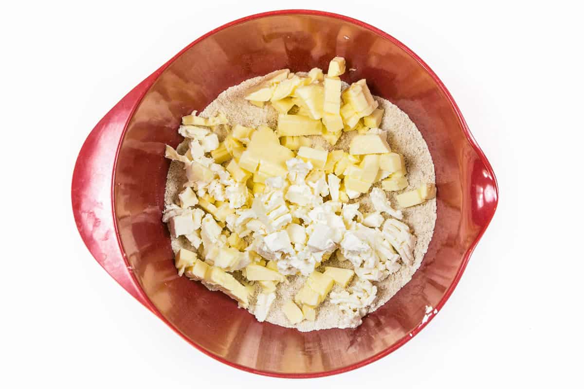 Slice one half cup of unsalted butter and four ounces of cream cheese, both that have softened at room temperature, into pieces, then add the butter and cream cheese together with the flour mixture.