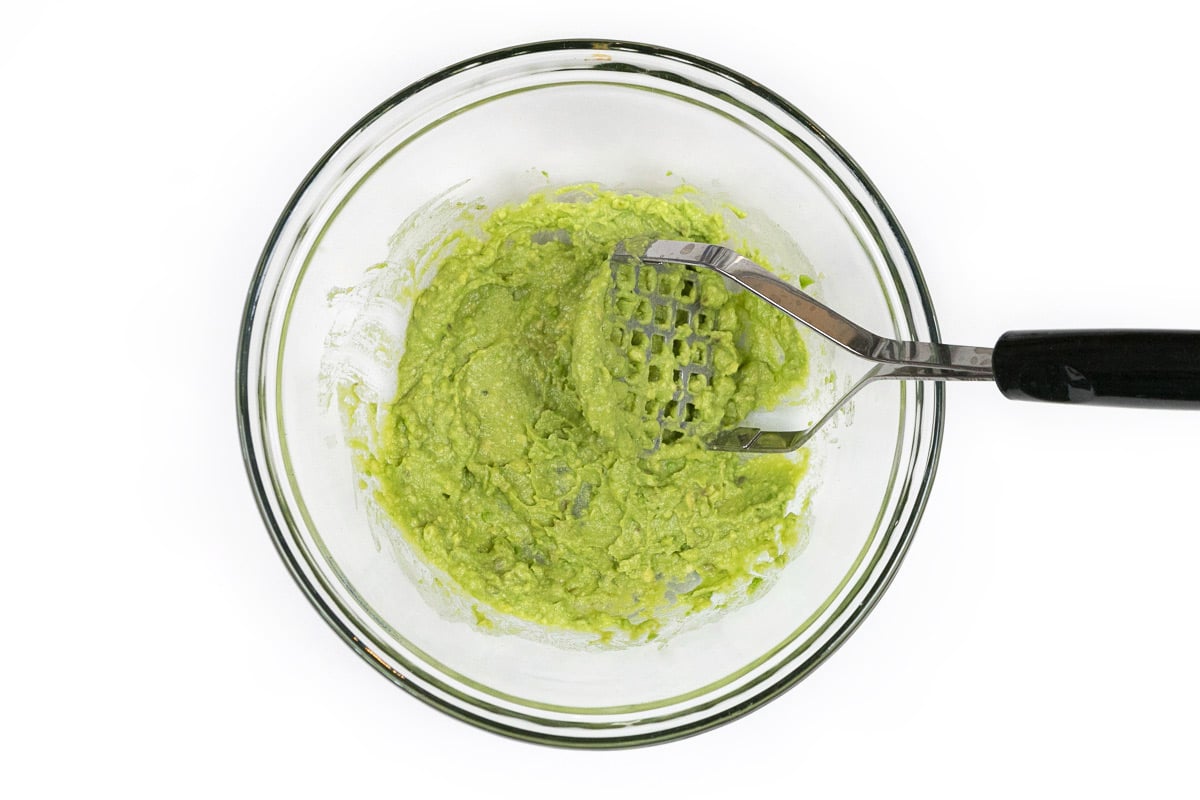 One avocado with the seed removed and mashed in a bowl.