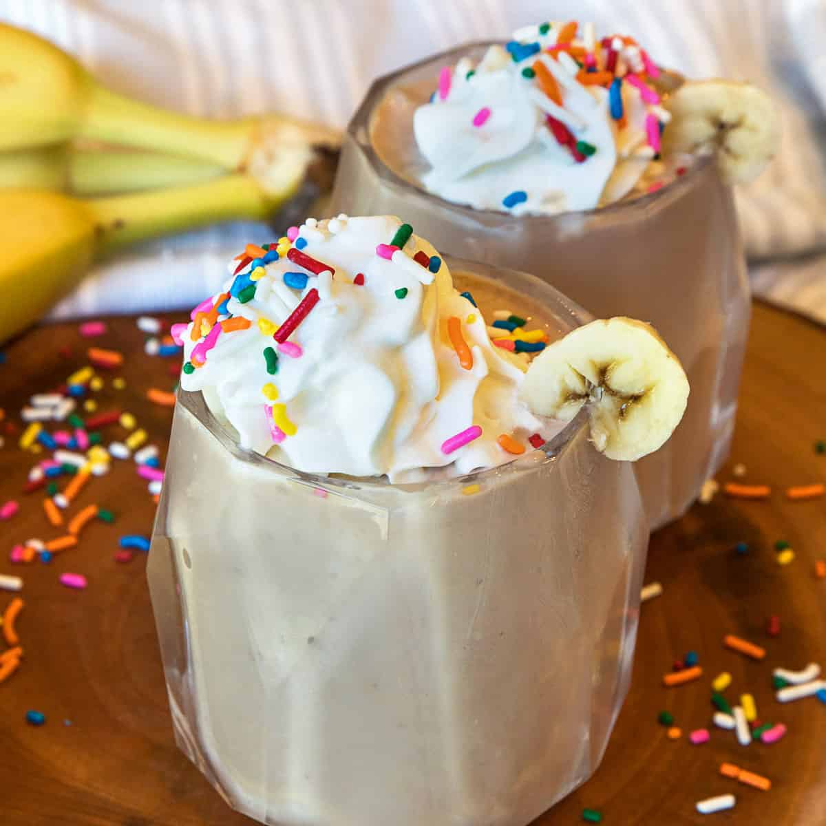 Banana chocolate milkshakes in a cup topped with whipped cream and sprinkles.