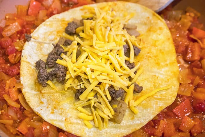 Ground beef mixture and cheese spread on a tortilla.
