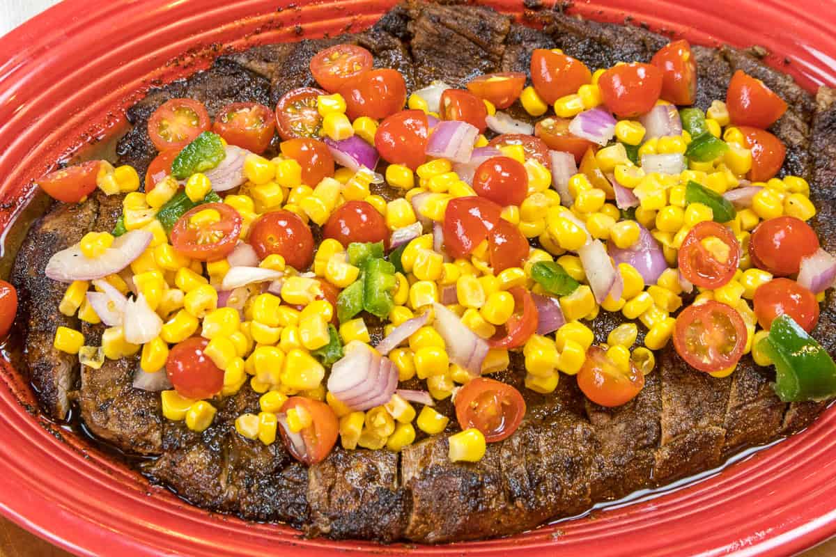 Broiled flank steak topped with roasted corn salsa on a plate.