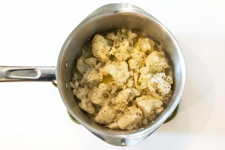 Buttered cauliflower in a saucepan, sprinkled with black pepper.