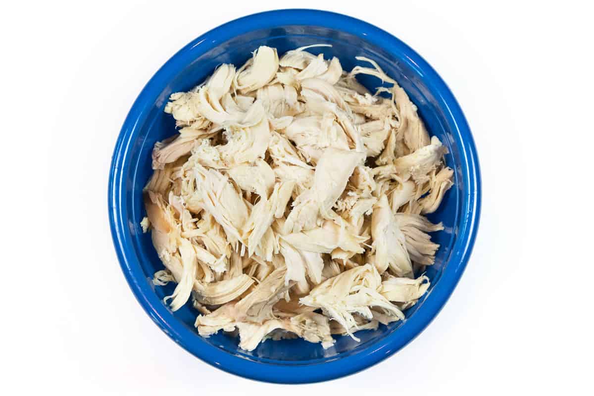 A rotisserie chicken is deboned and shredded in a bowl.