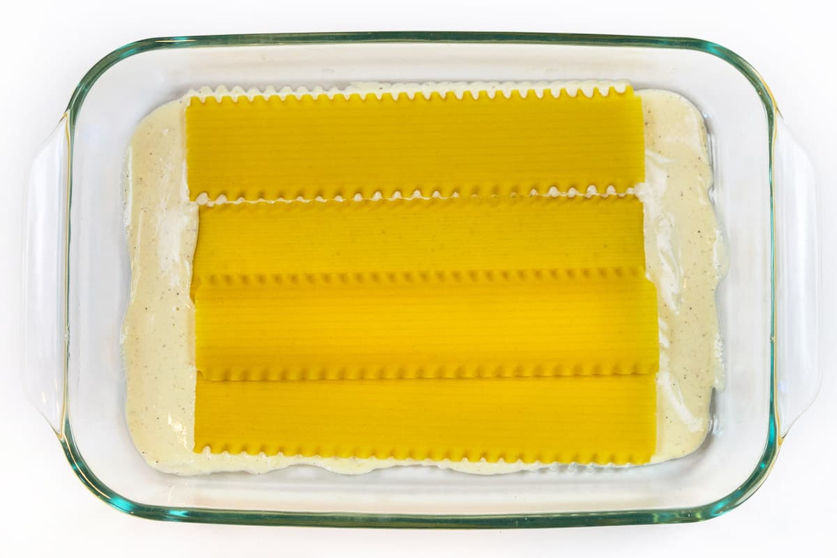 Four lasagna noodles on top of the Alfredo sauce.