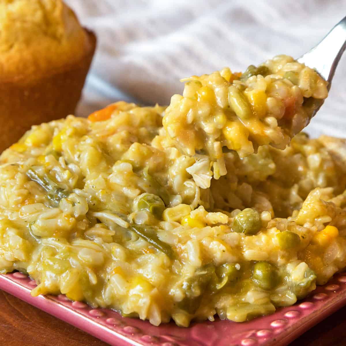 Cheesy chicken and rice casserole on a plate with cornbread in the background.