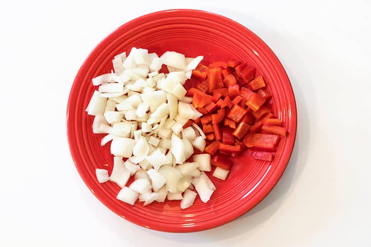 Diced onion and red bell pepper on a plate.