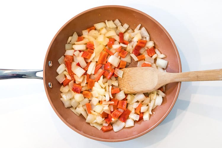 Sautéed onions and red bell peppers in a skillet.