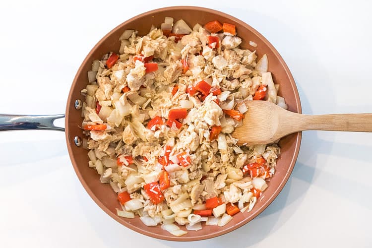 Shredded chicken, onions, and red bell peppers in a skillet.