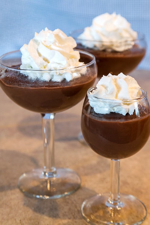 Homemade chocolate pudding in three bowls with whipped cream on top.