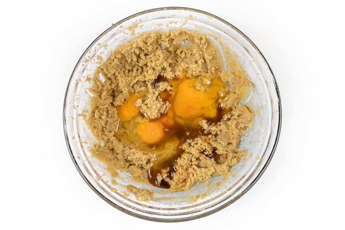The eggs and vanilla extract are added to the butter-sugar mixture in a bowl.