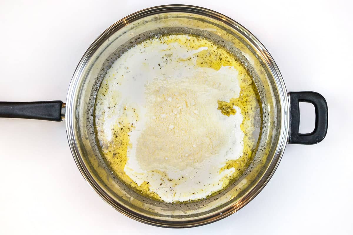 The heavy whipping cream and grated parmesan cheese are added to the butter and garlic mixture.