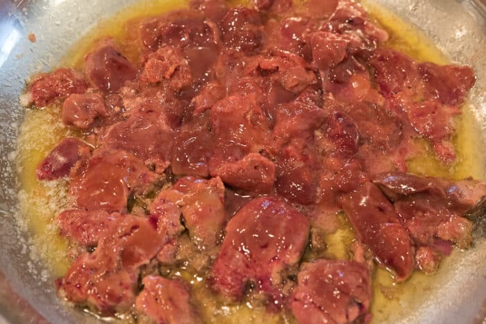 Raw cut up liver in a frying pan with the butter.