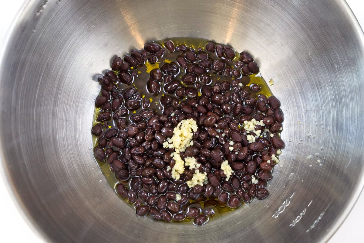 Olive oil, minced garlic, and black beans in a bowl.