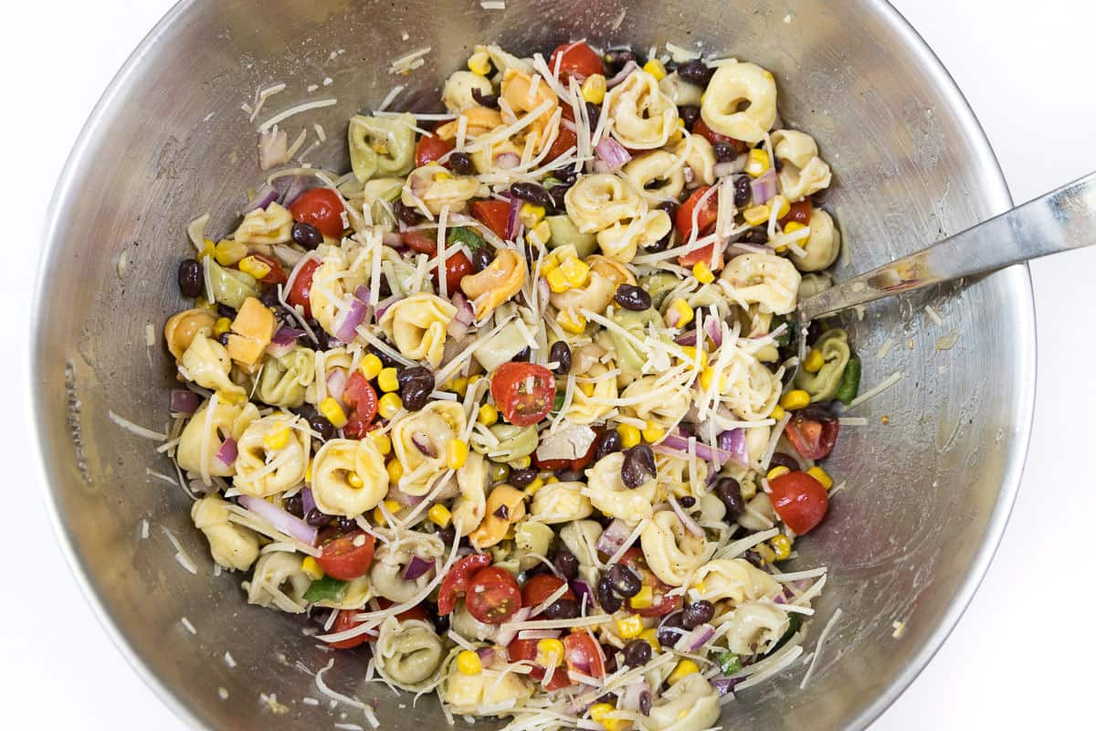 The shredded parmesan cheese is sprinkled on the tortellini pasta salad with corn salsa.