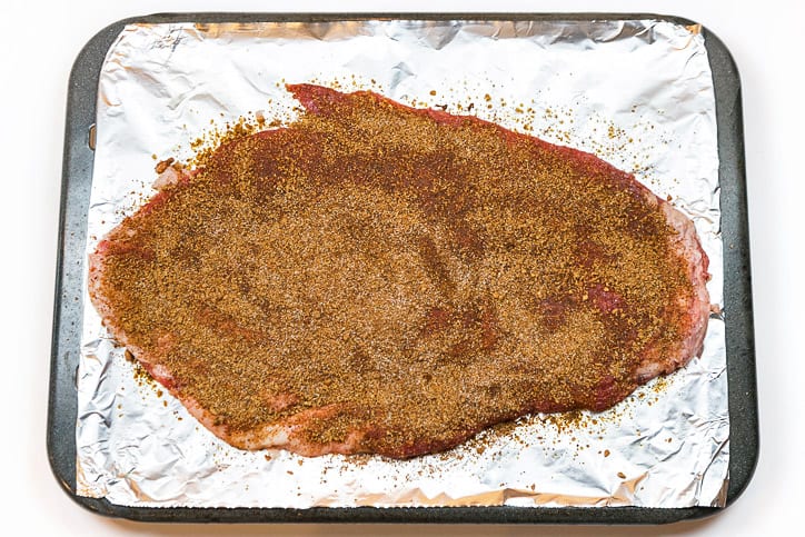 The dry rub seasoning mixture is spread on both sides of the flank steak.