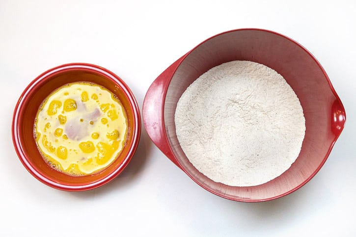 Two beaten eggs in a bowl, and the flour mixture in a bowl.