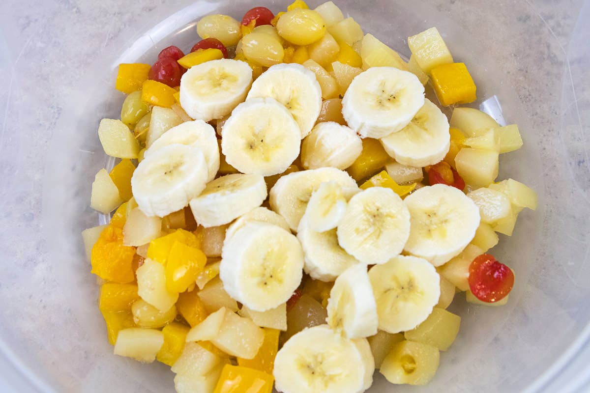 Bananas added to the fruit cocktail in a bowl.