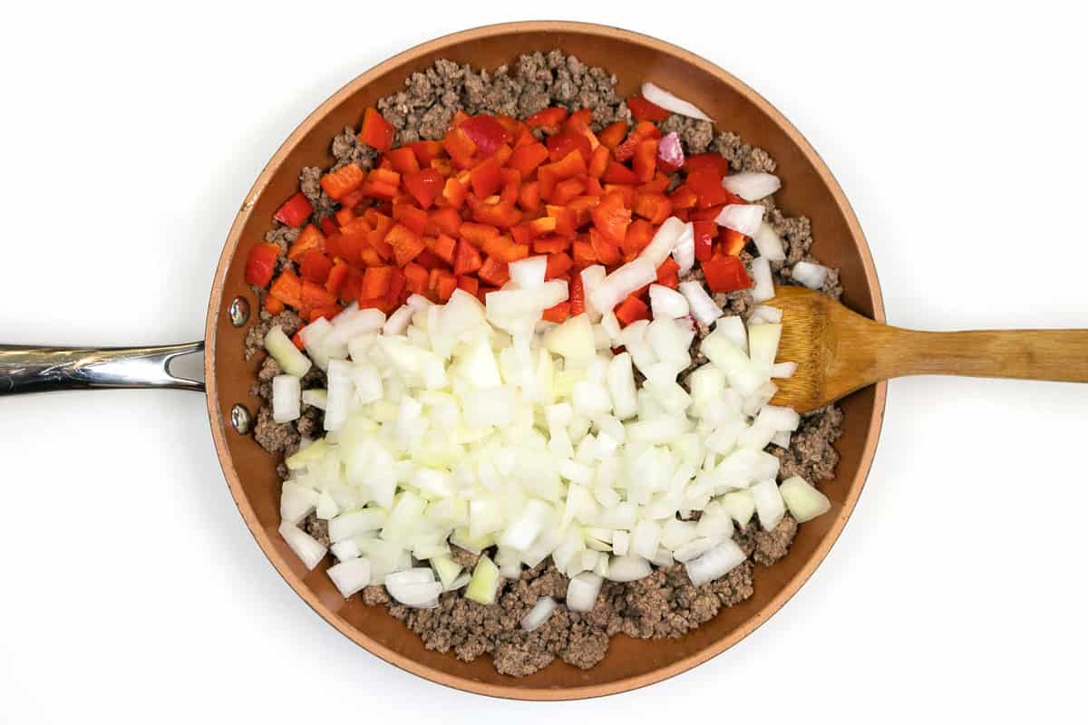 Diced red bell peppers and diced onions are added to the browned ground beef.
