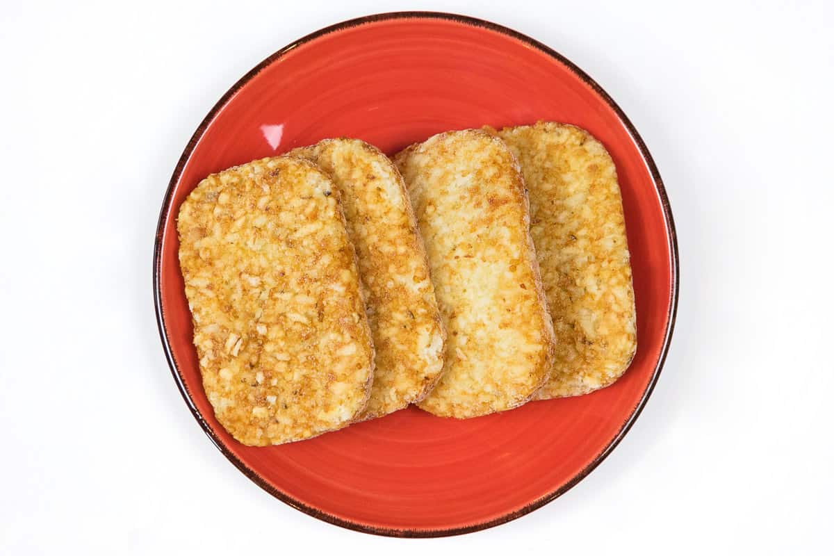 Four frozen hash brown patties on a plate.