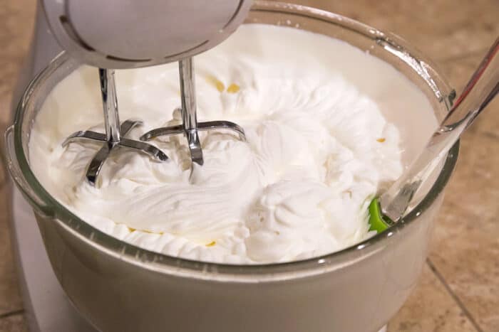 Whipping cream thicker and with peaks formed in a mixing bowl.