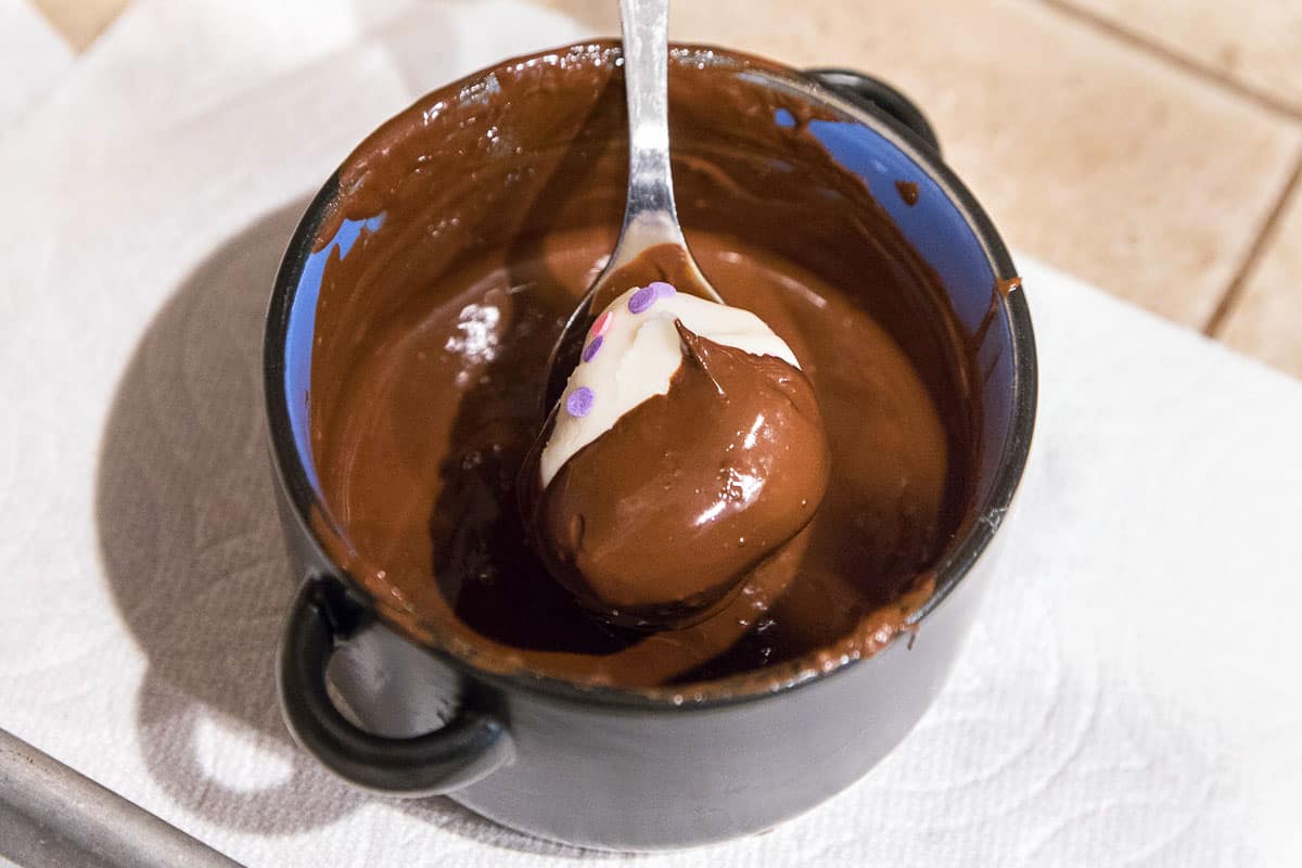 One marshmallow egg is dipped in melted chocolate baking bar.