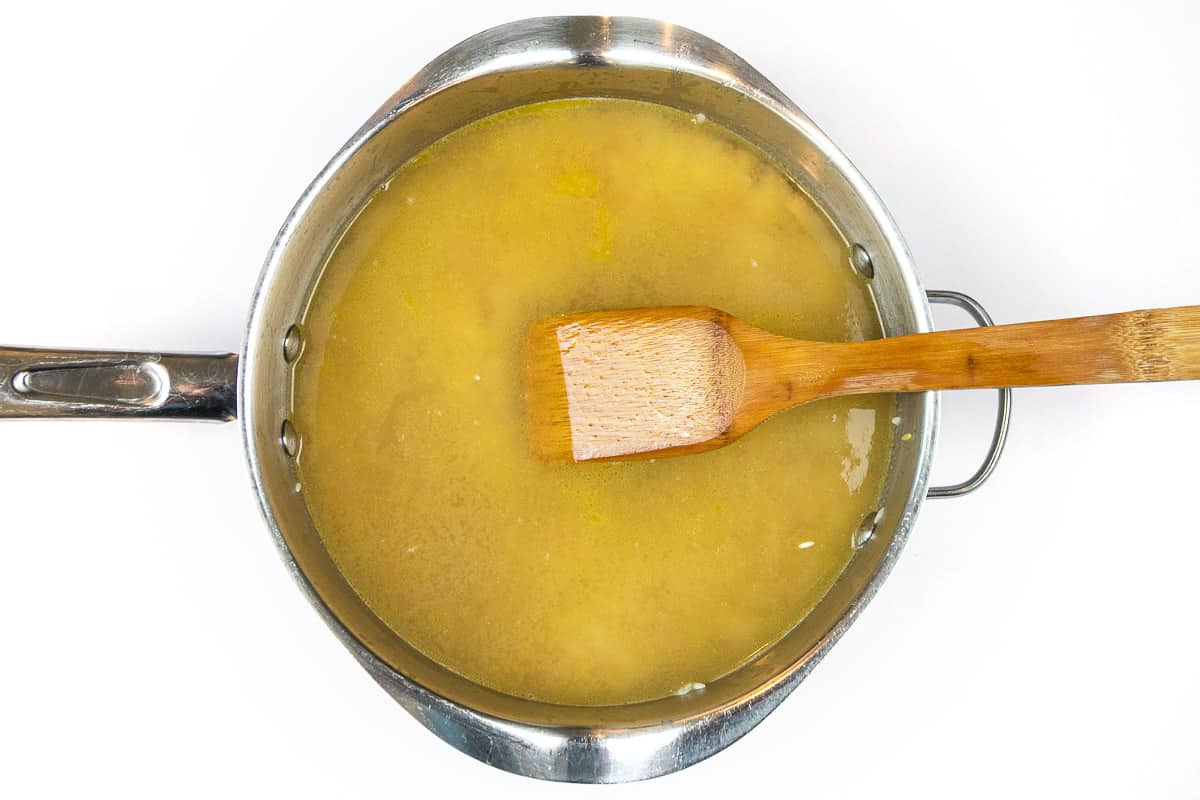 Add two cans of chicken broth to the browned long-grain rice and orzo pasta in a frying pan.
