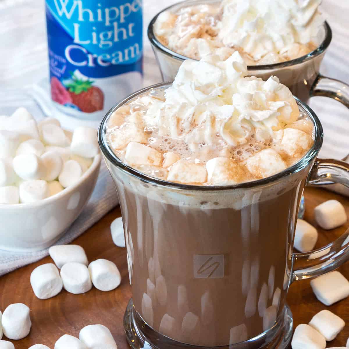 Two cups of hot chocolate with marshmallows and whipped cream on top.