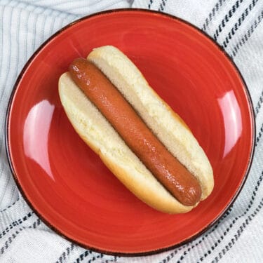 Microwaved hot dog on a red plate in a bun.