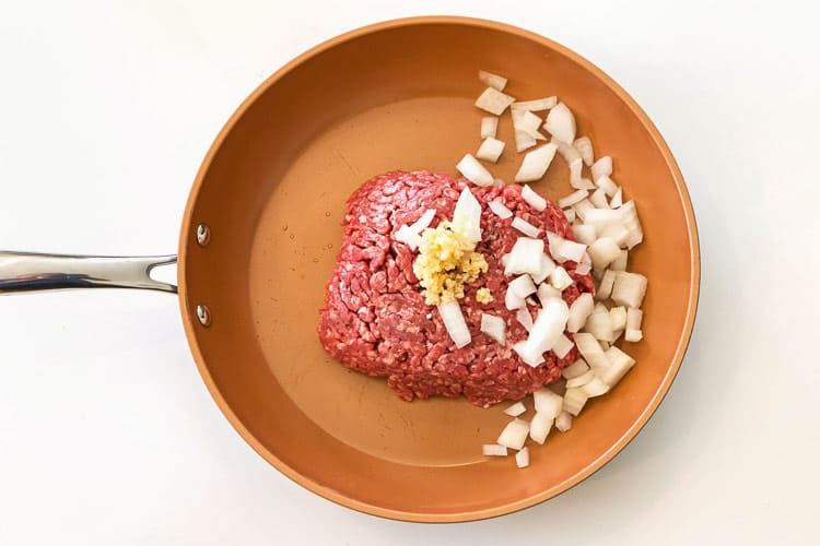 Lean ground beef, onions, and minced garlic in a frying pan.