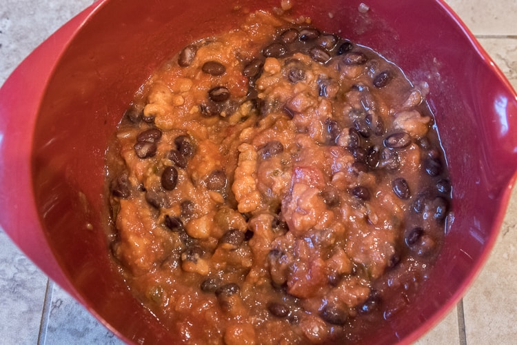 Black beans added together with the salsa and refried bean in a bowl.