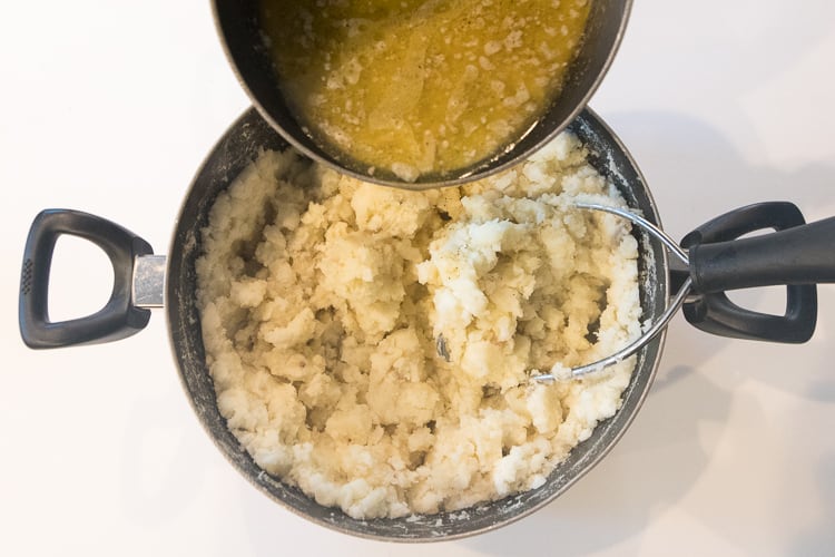 Adding the butter, whole milk, salt and pepper to the mashed potatoes.