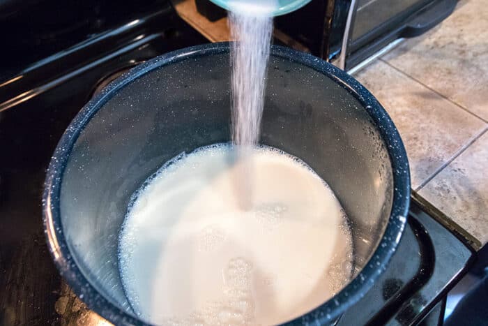 Three cups of milk in a pot and two tablespoons of sugar are added to the milk.