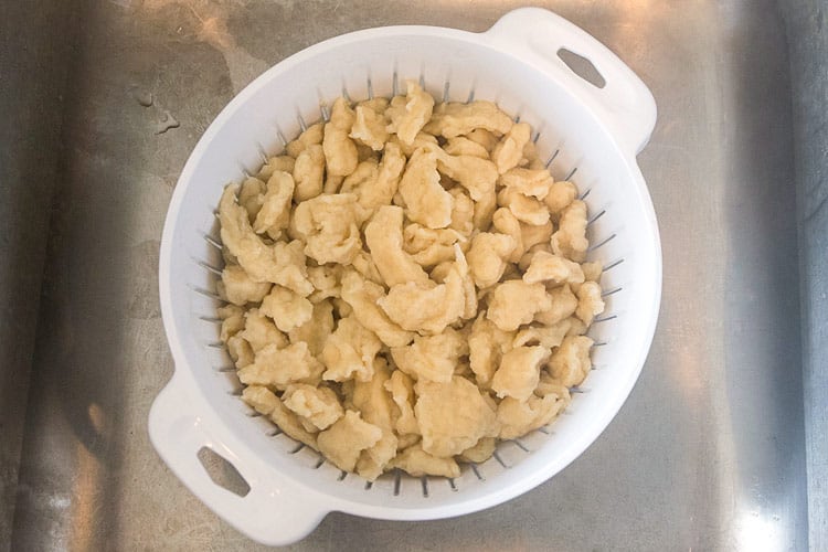 Dumplings in a colander, rinsed under cold water.