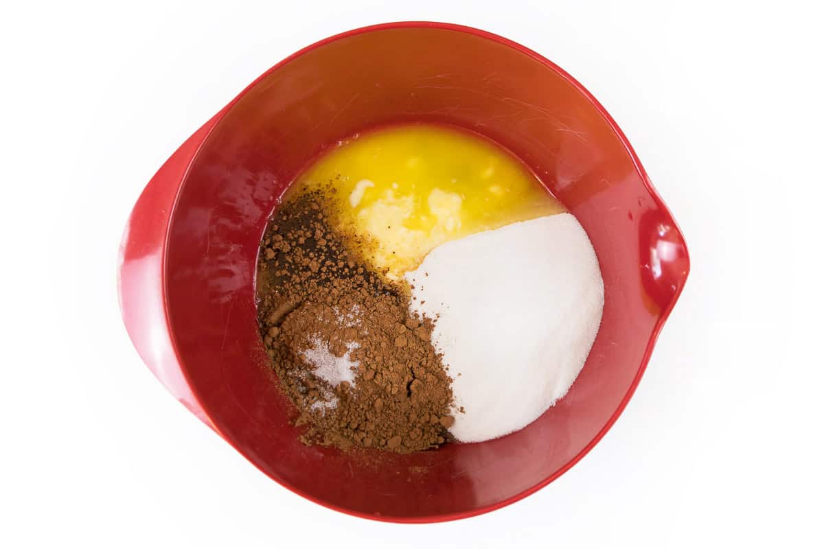 One cup of melted butter, two cups of granulated sugar, one-half cup of unsweetened cocoa powder, one-fourth teaspoon of salt, four eggs, and one teaspoon of vanilla extract in a bowl.