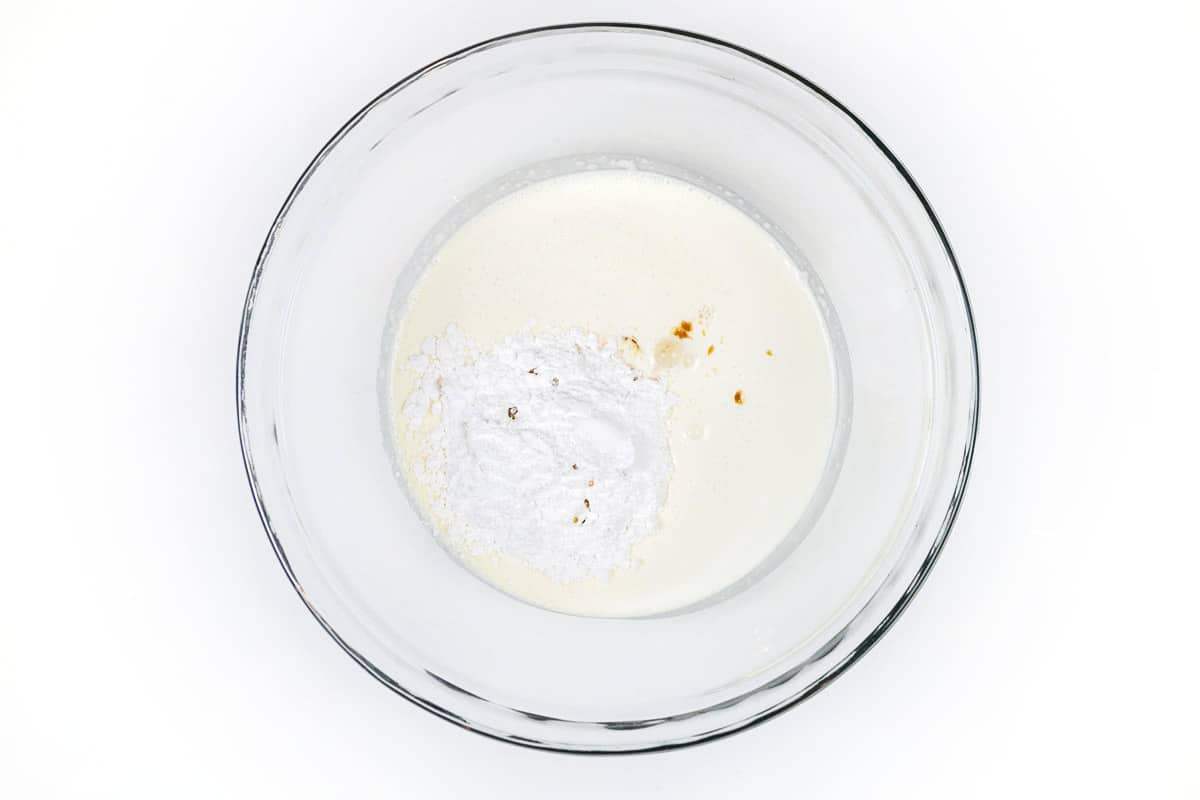 One and a half cups of heavy whipping cream, one fourth cup of powdered sugar, and one teaspoon of vanilla extract in a bowl.