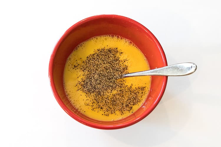 Six beaten eggs, salt, and pepper in a bowl.