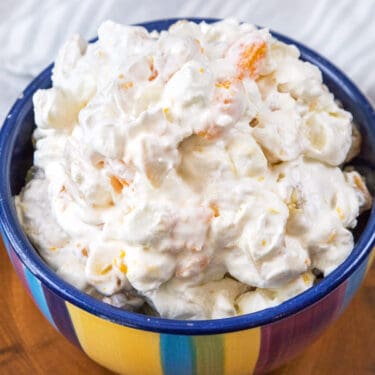 Fruit salad with cool whip recipe close up in a colorful striped bowl.