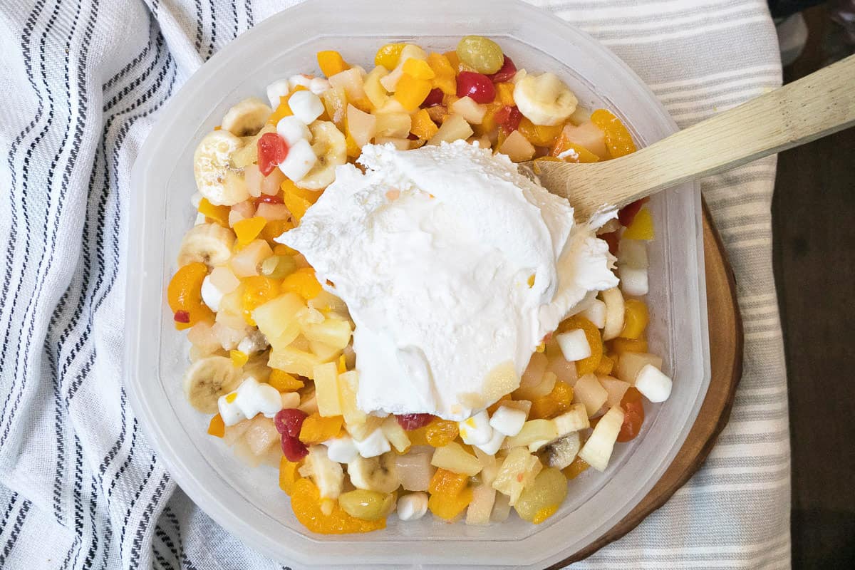 Cool whip is added to the bowl of fruit cocktail and bananas.