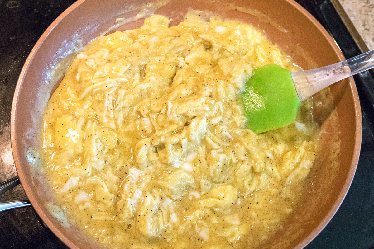 Eight scrambled eggs in a frying pan cooking.