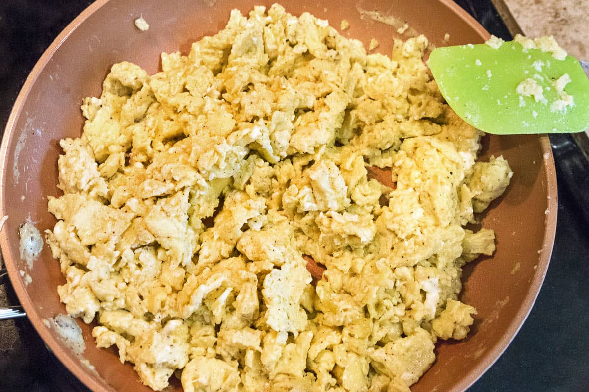 Eight scrambled eggs in a frying pan cooking.