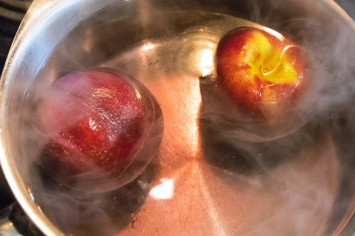 Boil water, then reduce the heat to simmer and put the peaches in the hot water for twenty seconds.