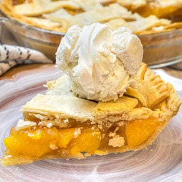 Close up of peach pie with canned peaches and ice cream on top.