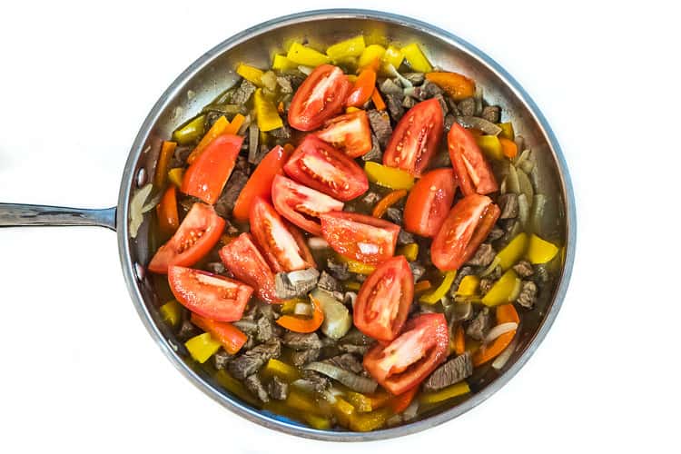 Tomatoes added to the steak mixture in the frying pan.